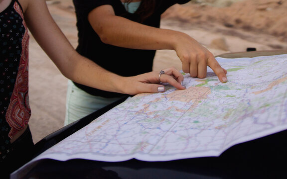 Hands point direction on a map spread on hood of vehicle