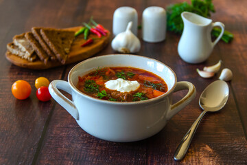 Borscht with sour cream in a beautiful white soup bowl on a wooden table. Traditional Ukrainian and Russian cuisine. 