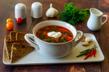 Borscht with sour cream in a beautiful white soup bowl on a wooden table. Traditional Ukrainian and Russian cuisine. 