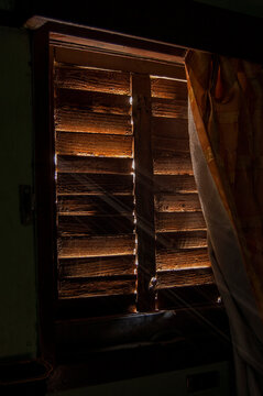 Sun rays seeping through the slits and cracks of a wooden window.