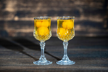 Homemade tincture of yellow cherry plum in a two wine crystal glass on wooden background, Ukraine