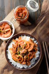 Stir fried kimchi with pork on cooked rice in a bowl on wooden background, Korean food