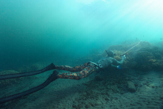 Camouflaged spear fisherman hunting fish deep at coral reef