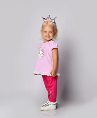 Small cute smiling blonde baby girl kid in pink stylish casual clothing and kitty ears stands side looking at camera