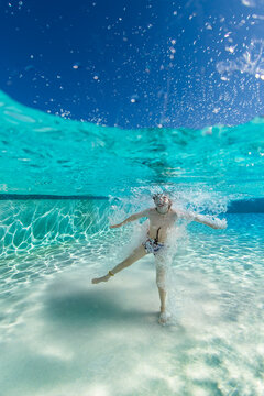 Over under image of a boy covered in water bubbles after jumping into a swimming pool