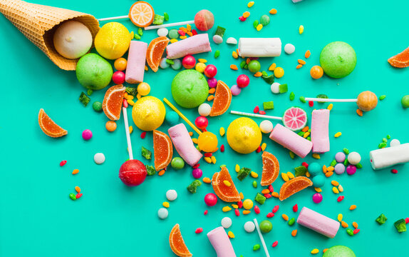 Colorful explosion of candies in ice cream cornet on turquoise background.