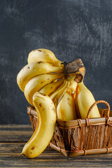 Bananas in a basket on wooden and plaster background. side view.