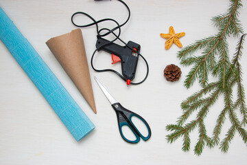 Making a Christmas tree out of paper. Scissors, hot glue gun, blue paper, cone and fir branches on a light table. An original children's art project. DIY concept.  Step 1.