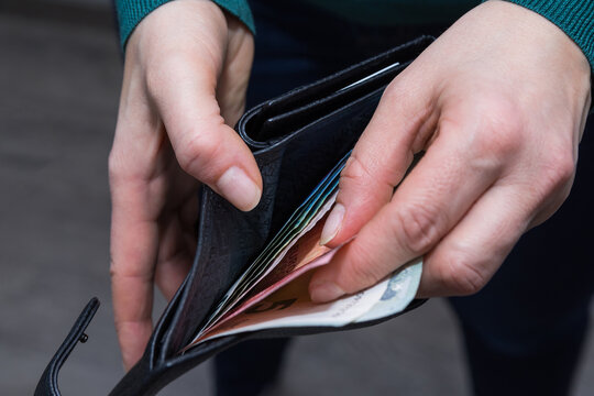 Closeup photo of woman hands, holding a good black leather wallet with some euro banknotes inside.