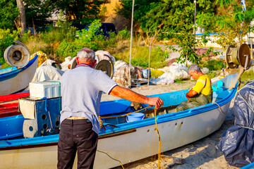 Obraz premium Two fishermen pile up fishing net on the sandy beach