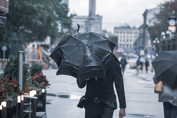 A businessman in a suit shelters an umbrella from the rain and wind outside in bad weather.