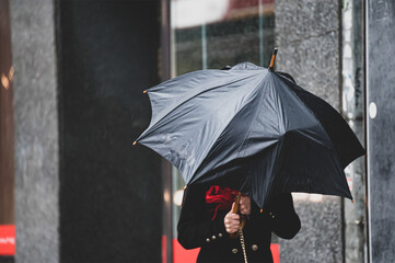 A woman has difficulty holding an umbrella from strong winds in rainy weather.