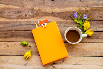 notebook planner for business work with hot coffee, yellow flowers ylang ylang arrangement flat lay style on background wooden