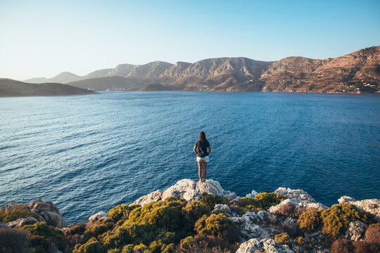Woman on a rocky outcrop overlooking an expansive sea view at sunset