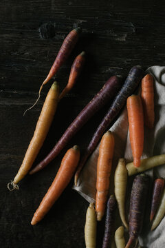 Harvest tricolor carrots on linen dish towel and dark wood table background