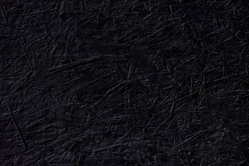 Black chipboard wall with shades of deep purple color. Horizontal background, copy space. Abstract texture surface made from pressed sawdust, paint to create atmosphere of magic, mystery. Dark moody