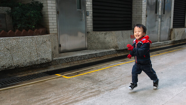 A young kid wearing cold weather clothes running happily in an alley