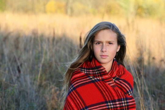 A Pretty Girl Standing In An Autumn Field Wrapped In A Warm Plaid Blanket