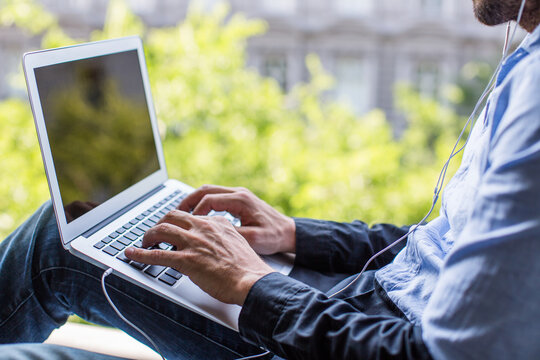 Man working on a laptop from home, sitting on a windowsill