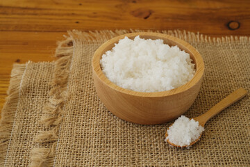 Flower of salt, is a salt that forms as a thin, delicate crust on the surface of seawater in the wooden bowl on sackcolth and wooden background. Called Fleur de sel in French. Selective focus