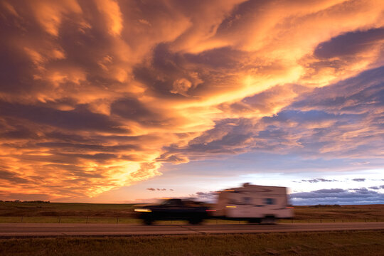 A truck towing a camper drives by with an impressive sunset