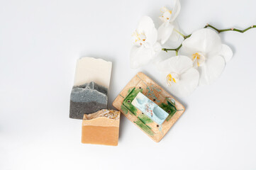 Natural handmade soap bar in ceramic soap dish with orchid flowers on white table