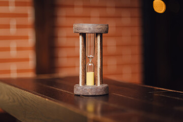 Vintage wooden hourglass against brick wall background. Time is running out