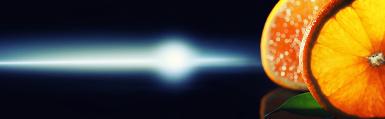 Composition with orange and grapefruit slices on a black background. A slice of orange with back light on a black background with water drops. Juicy orange on a table.