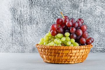 Grapes in a wicker basket on grungy grey and plaster background. side view.