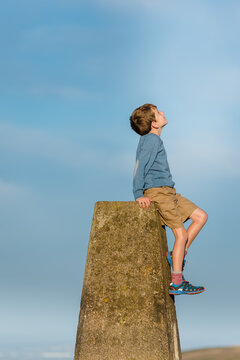Child sitting on trig point pillar looks up at the sky
