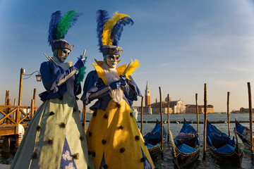 The Carnival of Venice: Molo San Marco, Venice, Italy. Masked revellers pose in front of the Basin of St Mark, with gondolas and the Chiesa di San Giorgio Maggiore in the background