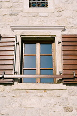 Close-up of a brown window with wooden shutters and a plank on the wall of a stone house.