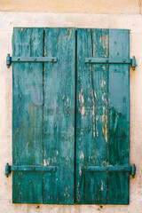 Old closed green wooden shutters with peeled paint.