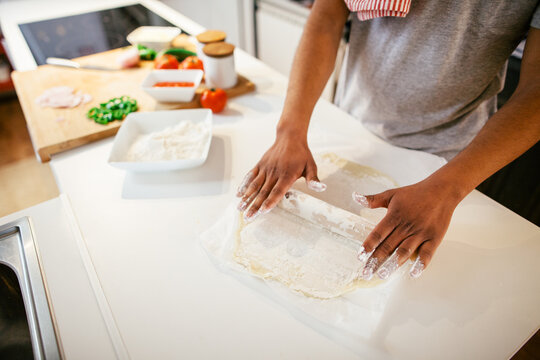 Closeup of a man rolling dough with a rolling pin in the kitchen.