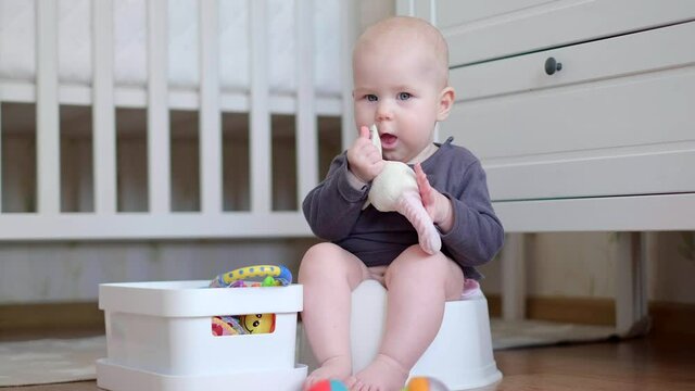 Newborn baby sitting on the potty and playing with toys