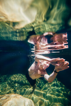 Man swims underwater in crystal clear fresh river water rockpool