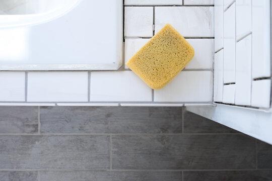 A sponge sits atop a newly tiled bathtub surround awaiting grout