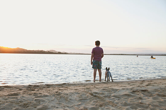 A young boy at the beach during sunset with his puppy