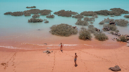 Couple standing on red sand beach and turquoise water