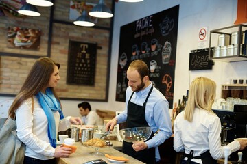 Waiter standing behind counter, serving female guest in cafeteria.
