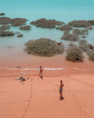 Couple standing on red sand beach and turquoise water
