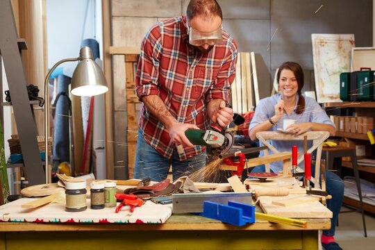 Man using hand saw, woman watching from background.