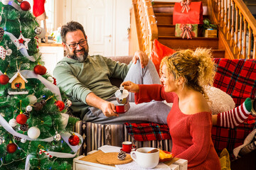 Christmas time at home with happy adult caucasian couple having breakfast on the couch near the...