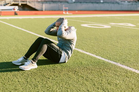 Athletic Man Doing Abdominal Crunches On Turf Field During Workout Routine
