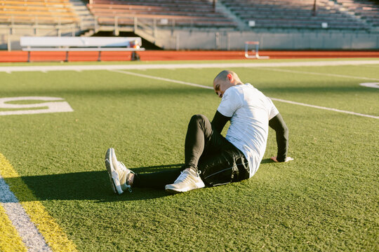 Athletic Man Stretching On Track and Turf Field During Workout