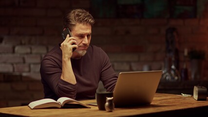 Older man tele working with laptop computer at home office in dark room, thinking, looking busy. 