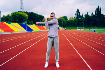 Strong caucasian male in activewear doing warming exercises for upper body preparing for workout, handsome hipster guy keeping healthy lifestyle reaching fitness goals and keeping perfect body shape