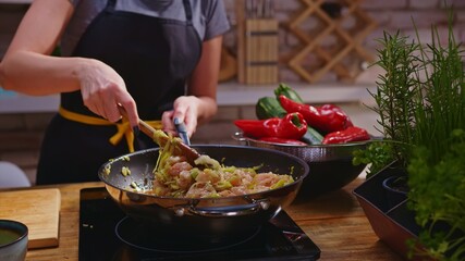Woman cooking frying chicken meat in wok pan on kitchen table. Closeup hands. Cosy dark room. Real, authentic cooking. 