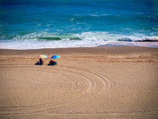 Fototapeta na wymiar Dos turistas disfrutan en la orilla de una playa malagueña desierta bajo sus parasoles de colores 