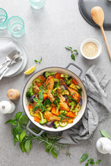 Chicken drumsticks roasted with vegetables in cast iron pan on kitchen table, top down view